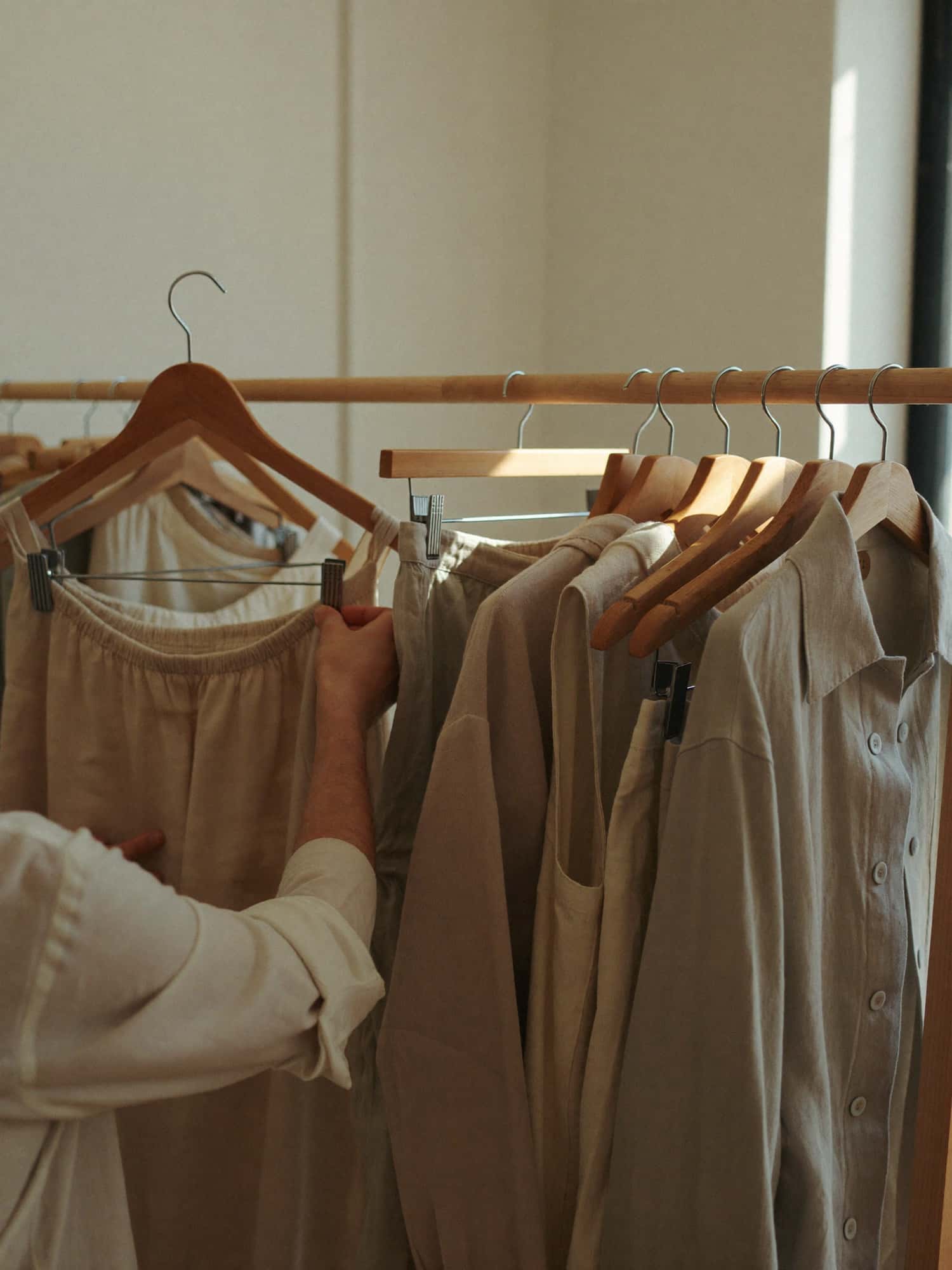 Neutral linen garments hanging on wooden racks in a sunlit boutique interior